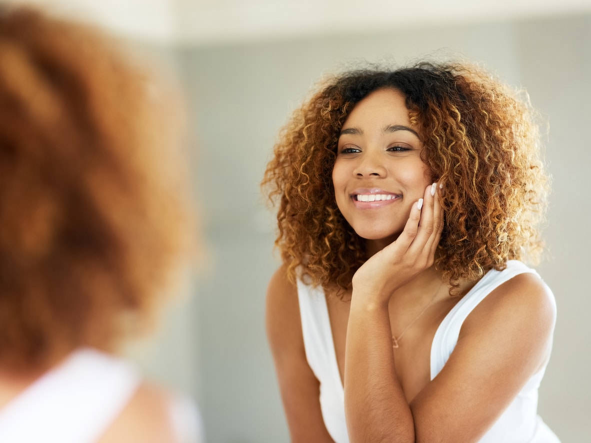 Photogenic woman with curly hair and light brown highlights examining her smile in the mirror