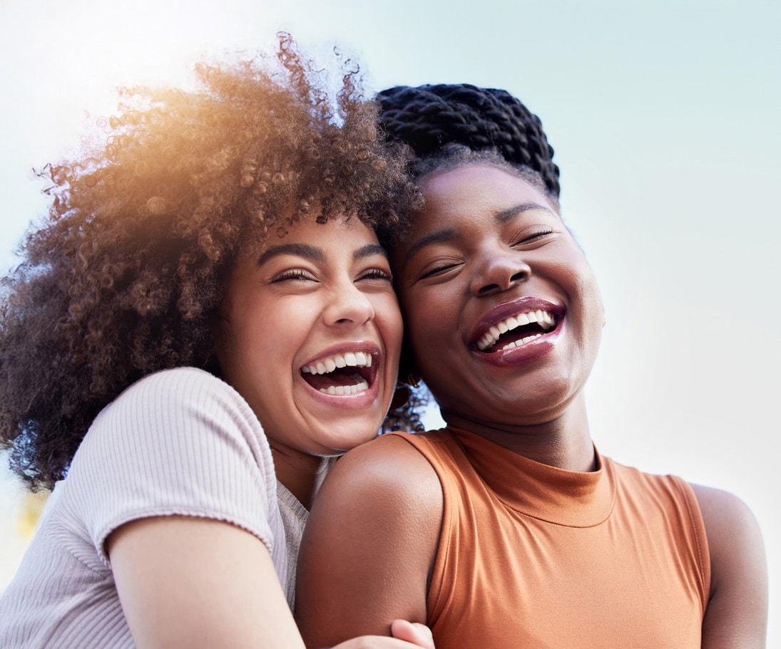 Two photogenic women laughing and embracing each other as summer sunlight reflects off their skin