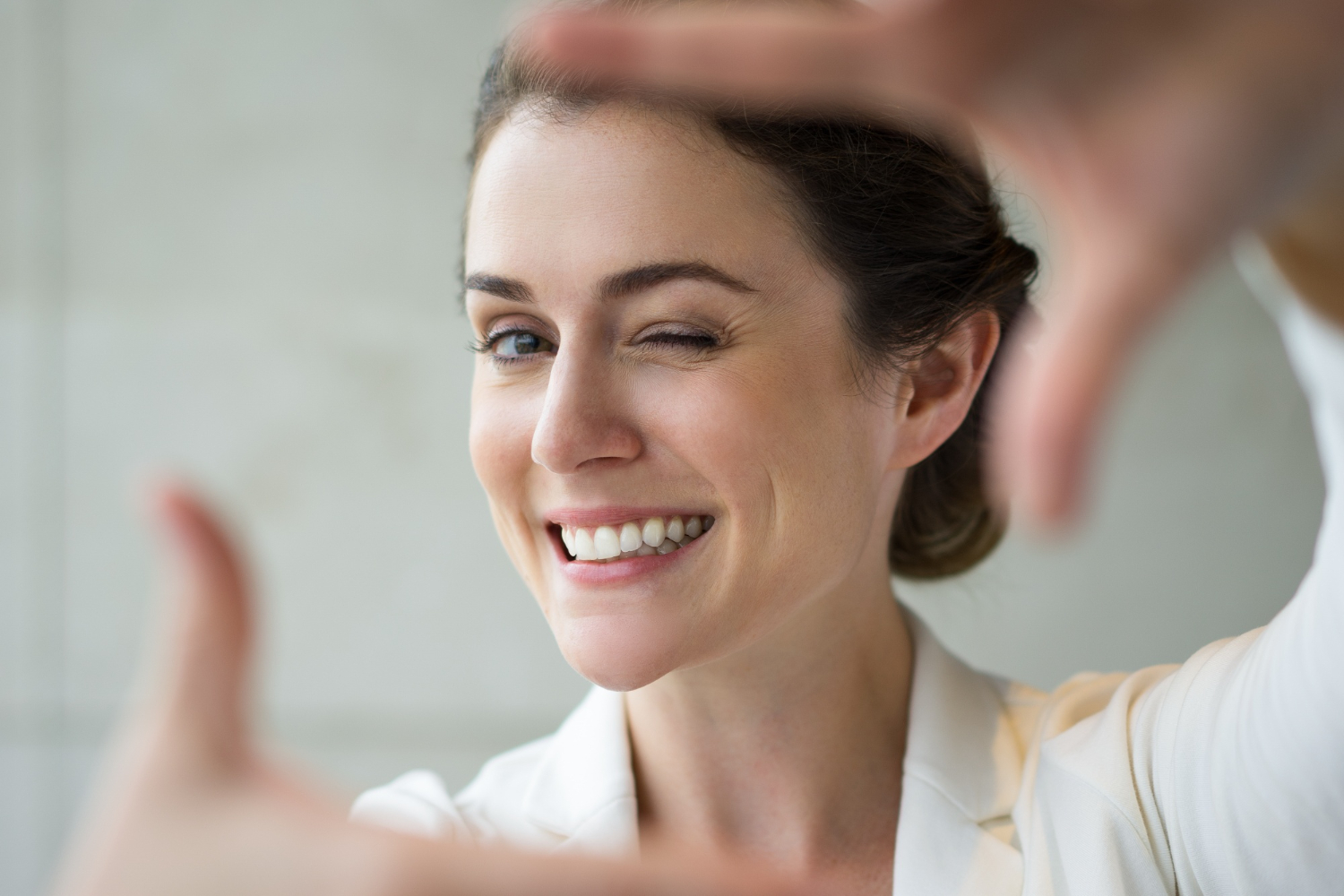 Woman smiling with one eye closed while framing her face with her hands