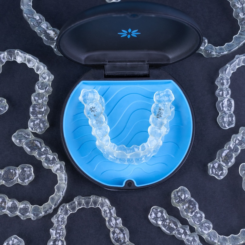Invisalign® aligner in a sleek light and dark blue Invisalign case surrounded by other aligners