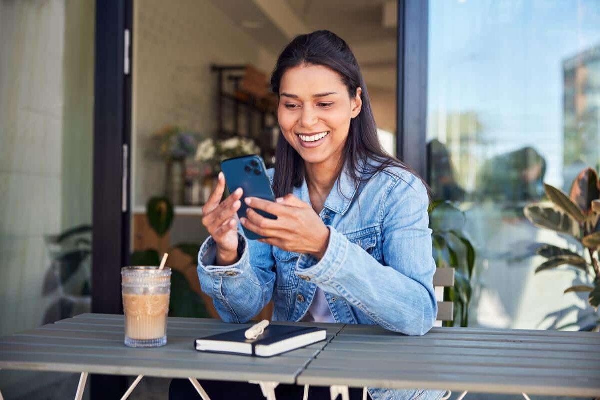 young woman smiling online phone outside coffee shop happy e1705457233262
