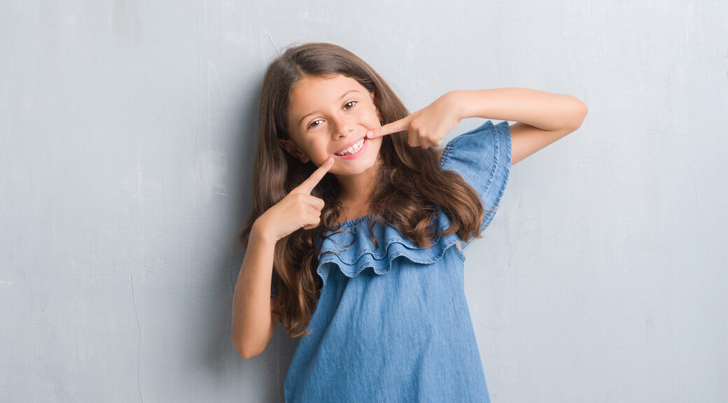 Young hispanic kid over grunge grey wall smiling confident showing and pointing with fingers teeth and mouth. Health concept.
