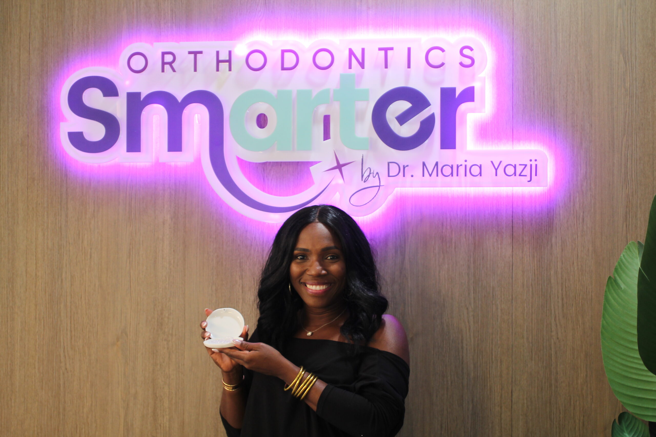 beautiful black woman holding invisalign in front of the smarter orthodontics neon sign
